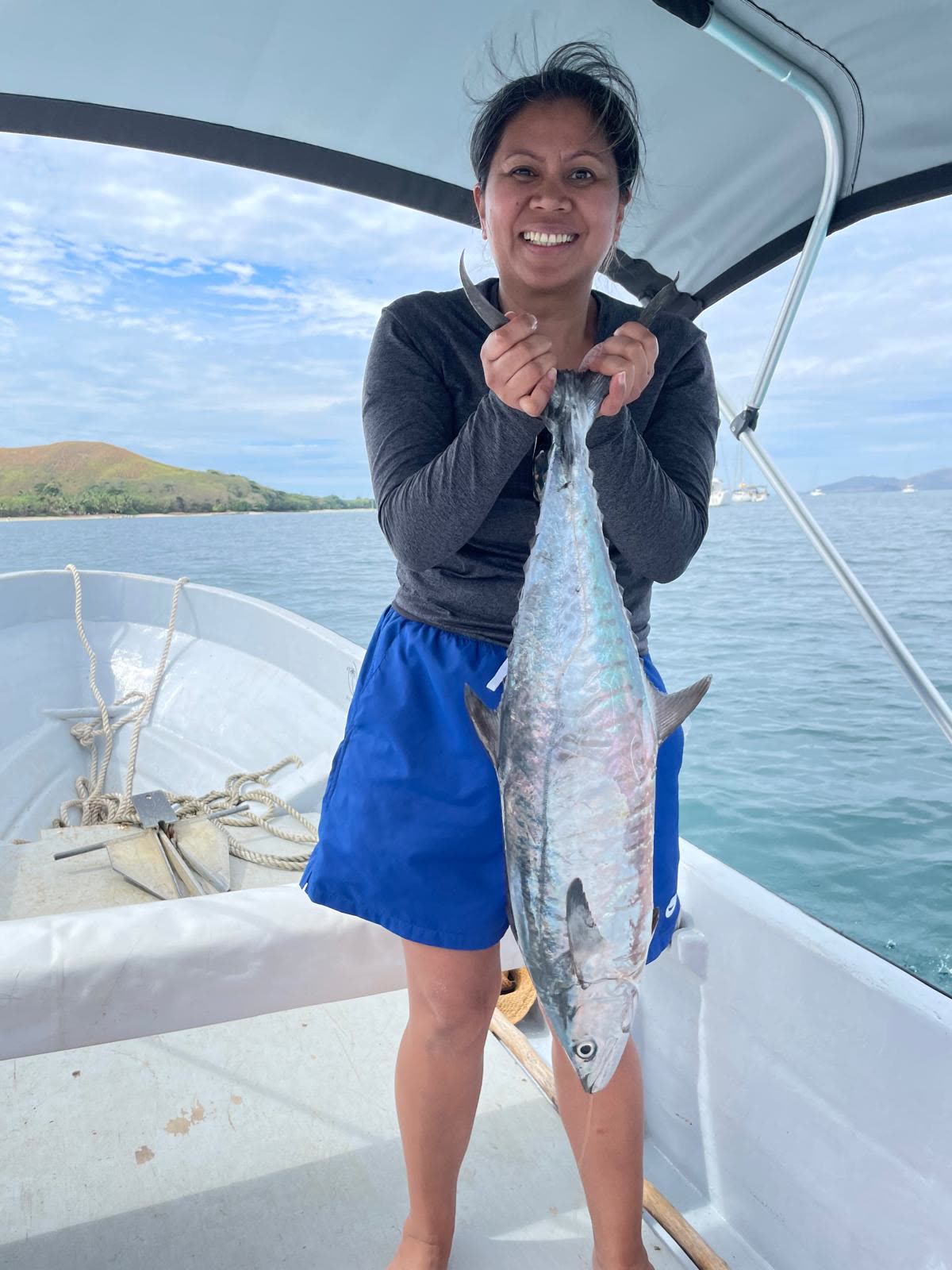 Guest smiling on the boat, holding up a freshly caught mackerel with a Fijian island behind
